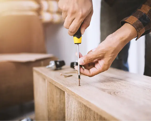 Nahaufnahme einer Hand, die mit einem Schraubendreher eine Schraube in ein Holzmöbel dreht, Symbol für Möbelaufbau, Montage-Service und hochwertige Verarbeitung von Wohnmöbeln.